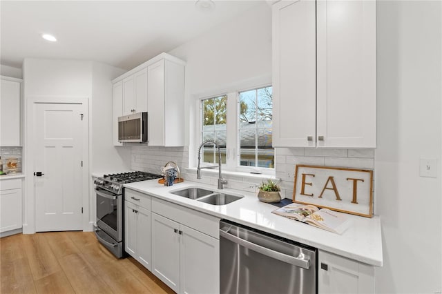 kitchen featuring sink, light hardwood / wood-style flooring, decorative backsplash, white cabinetry, and stainless steel appliances