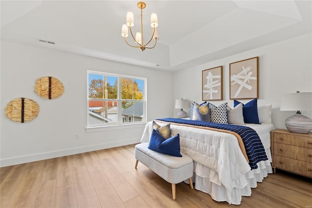 bedroom featuring a tray ceiling, a chandelier, and light hardwood / wood-style floors