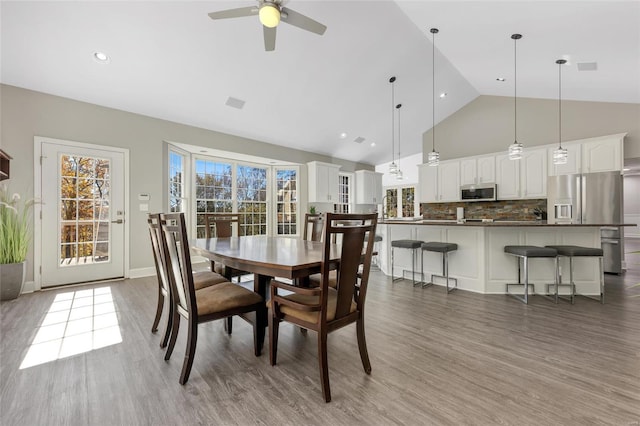 dining space with ceiling fan, wood-type flooring, and vaulted ceiling