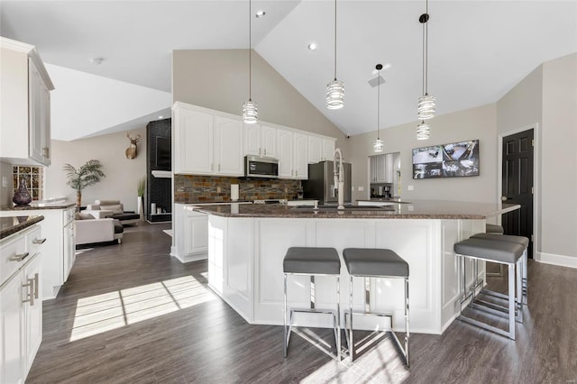 kitchen with backsplash, stainless steel appliances, a kitchen island with sink, white cabinets, and hanging light fixtures