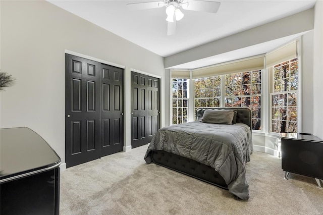 bedroom featuring two closets, light colored carpet, and ceiling fan