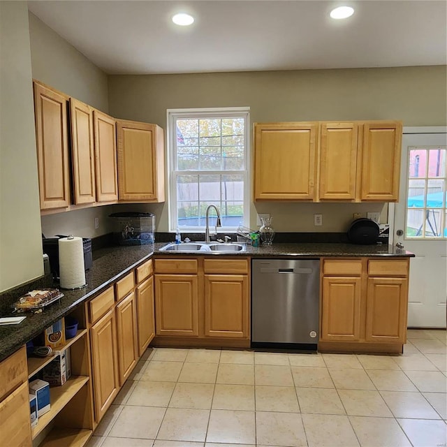 kitchen featuring stainless steel dishwasher, light tile patterned flooring, dark stone counters, and sink