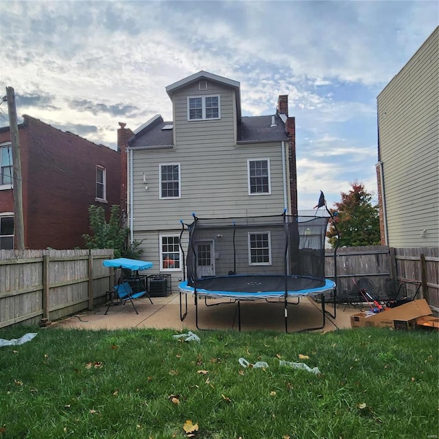 rear view of property featuring a patio area, cooling unit, a trampoline, and a yard