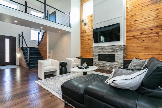 living room with dark hardwood / wood-style flooring, wood walls, a stone fireplace, and a towering ceiling