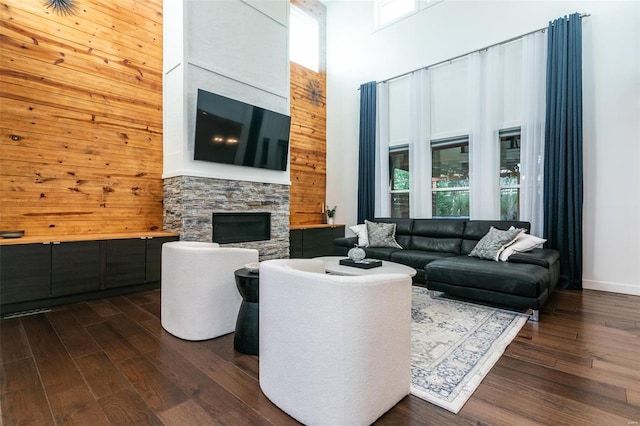 living room with a high ceiling, dark wood-type flooring, a stone fireplace, and wooden walls