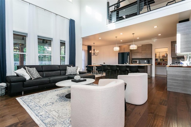 living room with dark wood-type flooring, a towering ceiling, and an inviting chandelier