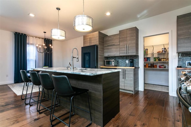 kitchen with hanging light fixtures, dark hardwood / wood-style floors, decorative backsplash, and black refrigerator