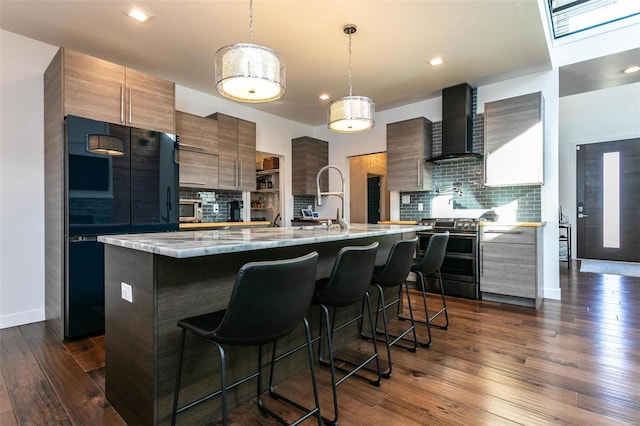 kitchen featuring dark hardwood / wood-style flooring, a kitchen island with sink, wall chimney exhaust hood, and stainless steel appliances