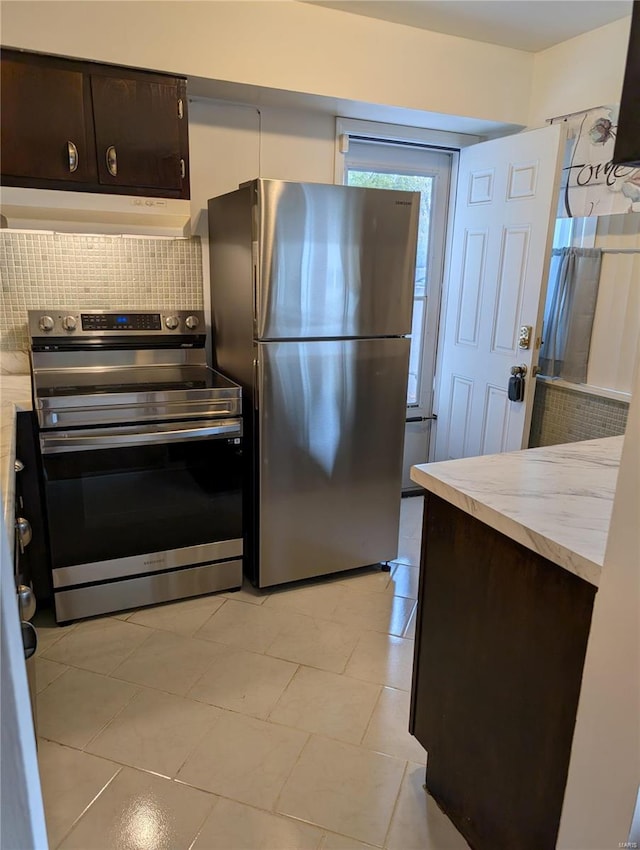 kitchen featuring stainless steel appliances, light tile patterned floors, backsplash, and dark brown cabinetry