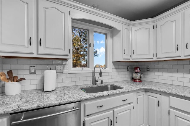 kitchen with light stone countertops, white cabinetry, dishwasher, and sink