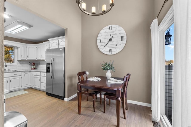 kitchen with stainless steel refrigerator with ice dispenser, white cabinetry, backsplash, a chandelier, and light hardwood / wood-style flooring