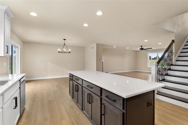 kitchen with light wood-type flooring, ceiling fan with notable chandelier, dark brown cabinetry, white cabinets, and hanging light fixtures