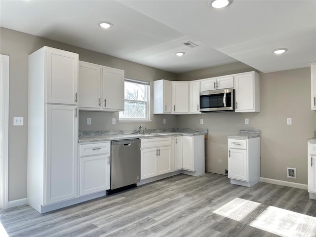 kitchen with light wood-type flooring, sink, stainless steel appliances, and white cabinetry