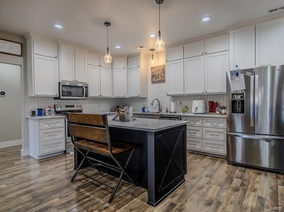 kitchen with white cabinetry, appliances with stainless steel finishes, hanging light fixtures, wood-type flooring, and a kitchen island