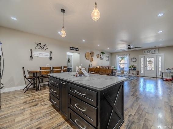 kitchen with light wood-type flooring, light stone counters, pendant lighting, and a kitchen island