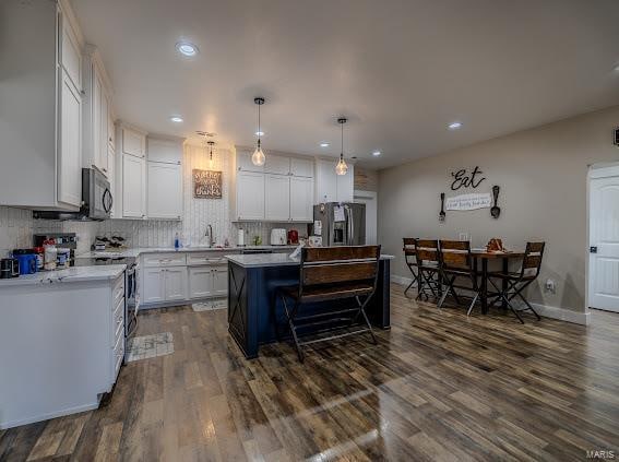 kitchen with appliances with stainless steel finishes, a center island, white cabinets, pendant lighting, and dark hardwood / wood-style flooring