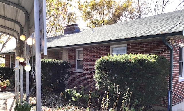 view of side of home featuring brick siding, a chimney, and roof with shingles