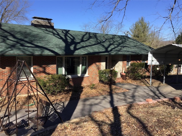 exterior space with a shingled roof, a detached carport, brick siding, and a chimney