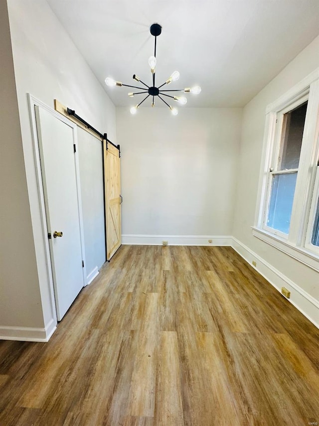 unfurnished bedroom featuring an inviting chandelier, a barn door, and hardwood / wood-style flooring