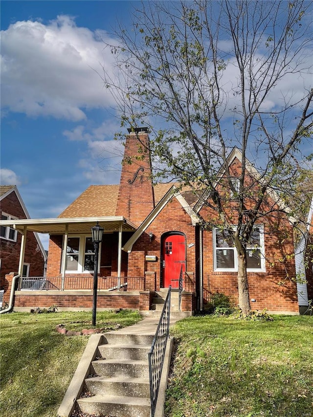 view of front of property with brick siding, a chimney, a front yard, and a shingled roof