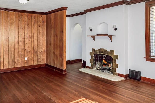 unfurnished living room with dark wood-style floors, arched walkways, ornamental molding, a warm lit fireplace, and baseboards