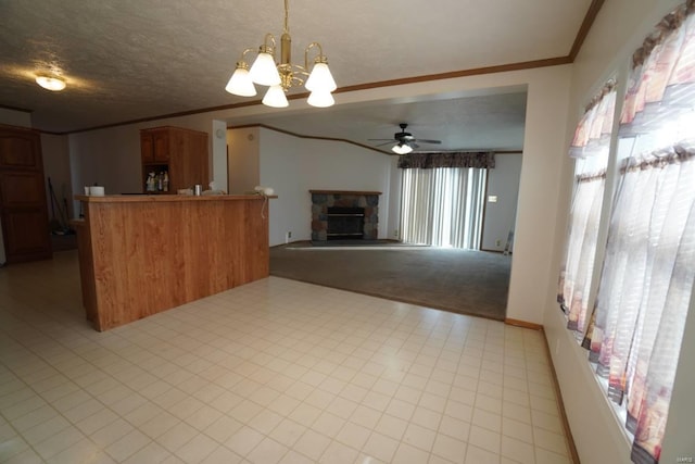 kitchen with crown molding, a stone fireplace, decorative light fixtures, kitchen peninsula, and ceiling fan with notable chandelier