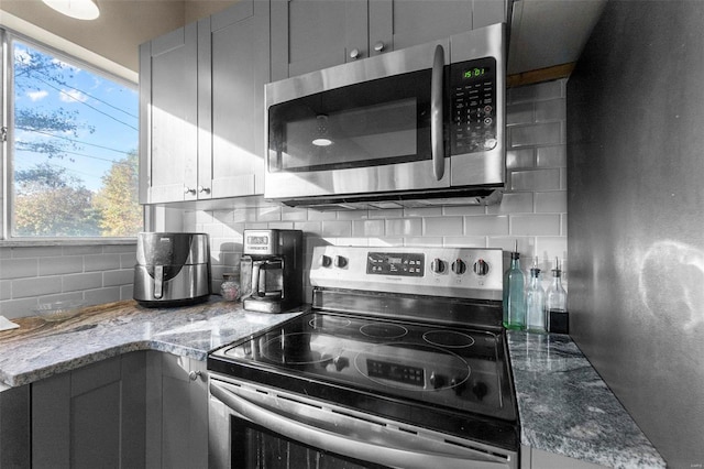 kitchen featuring appliances with stainless steel finishes, decorative backsplash, light stone counters, and plenty of natural light