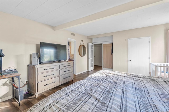 bedroom with dark wood-type flooring, a closet, beamed ceiling, and a barn door