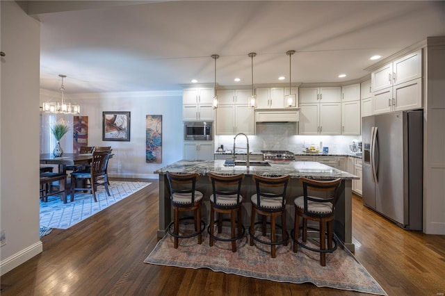 kitchen with sink, light stone counters, appliances with stainless steel finishes, decorative light fixtures, and dark hardwood / wood-style flooring