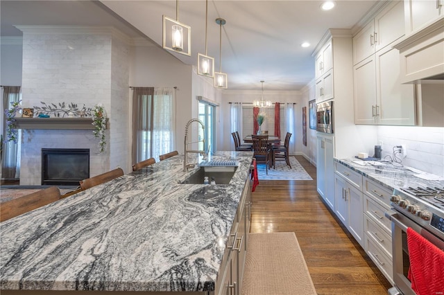 kitchen with dark hardwood / wood-style flooring, white cabinets, sink, an island with sink, and light stone countertops