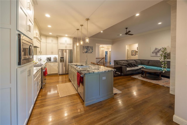 kitchen with stainless steel appliances, dark hardwood / wood-style floors, pendant lighting, white cabinets, and a kitchen island with sink