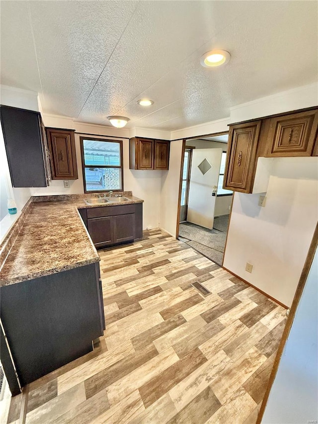 kitchen featuring dark brown cabinetry, light hardwood / wood-style floors, stone countertops, sink, and a textured ceiling