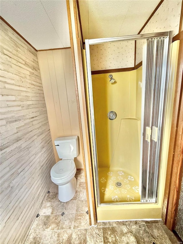 bathroom featuring toilet, wood walls, an enclosed shower, and a textured ceiling