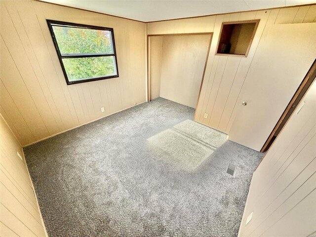 unfurnished bedroom featuring wooden walls, a closet, and carpet