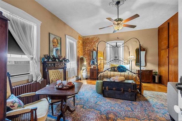 bedroom with hardwood / wood-style floors, radiator heating unit, ceiling fan, and brick wall