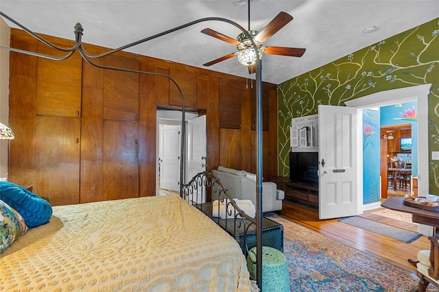 bedroom featuring hardwood / wood-style flooring, ceiling fan, and wood walls