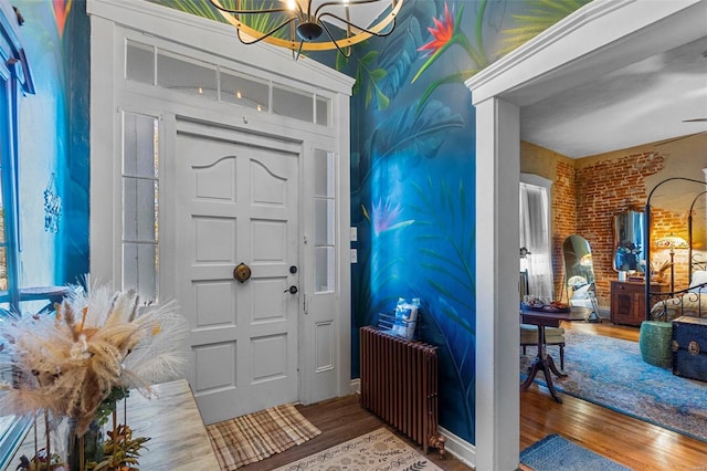 foyer entrance with hardwood / wood-style flooring, a notable chandelier, brick wall, and radiator