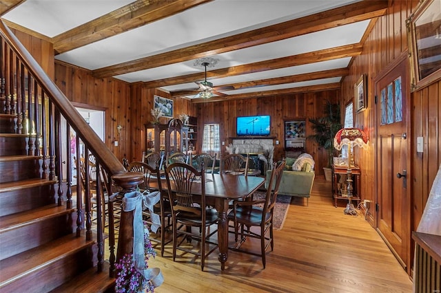 dining room featuring beam ceiling, ceiling fan, wooden walls, and hardwood / wood-style floors