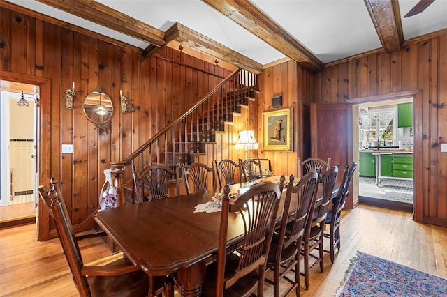 dining room with beamed ceiling, light hardwood / wood-style flooring, and wood walls