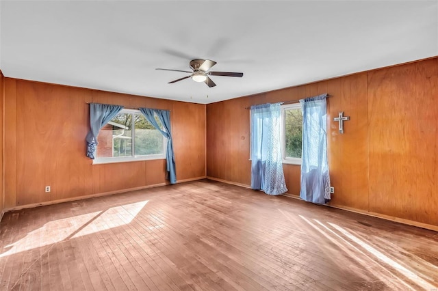 unfurnished room with a wealth of natural light, wooden walls, light hardwood / wood-style floors, and ceiling fan