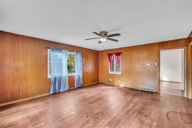 unfurnished room featuring hardwood / wood-style floors, ceiling fan, and wooden walls