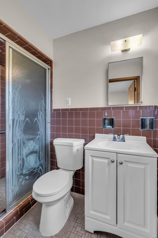 bathroom with tile walls, vanity, toilet, and a shower with shower door