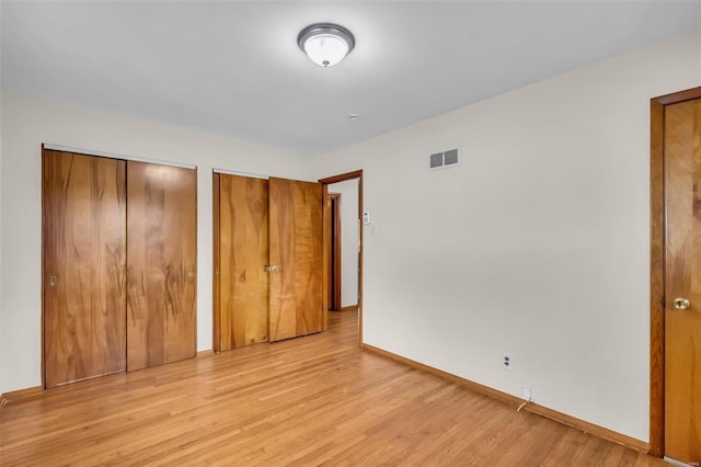 unfurnished bedroom with light wood-type flooring and two closets