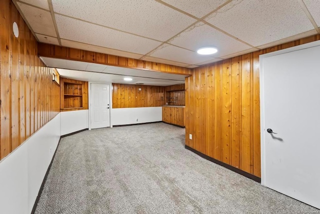 basement featuring carpet, a paneled ceiling, and wood walls