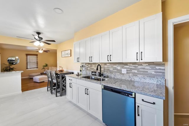 kitchen featuring decorative backsplash, light stone counters, stainless steel dishwasher, sink, and white cabinetry