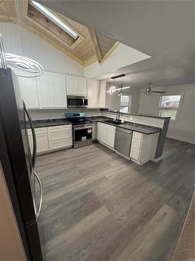 kitchen featuring lofted ceiling with beams, kitchen peninsula, appliances with stainless steel finishes, decorative light fixtures, and wood-type flooring