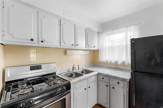 kitchen with black refrigerator, backsplash, gas stove, sink, and white cabinets