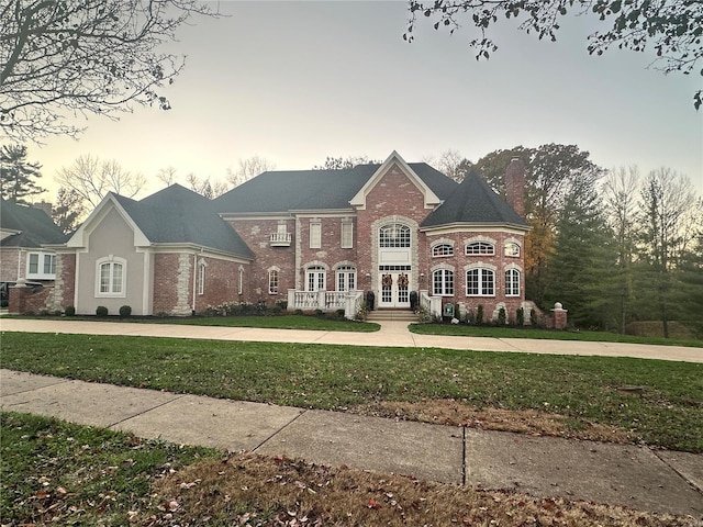 view of front of property featuring a chimney, a lawn, and brick siding