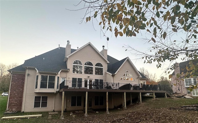 back of property at dusk with brick siding, a chimney, and a wooden deck