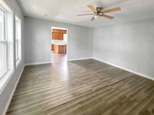 spare room featuring a healthy amount of sunlight, dark wood-type flooring, a textured ceiling, and ceiling fan